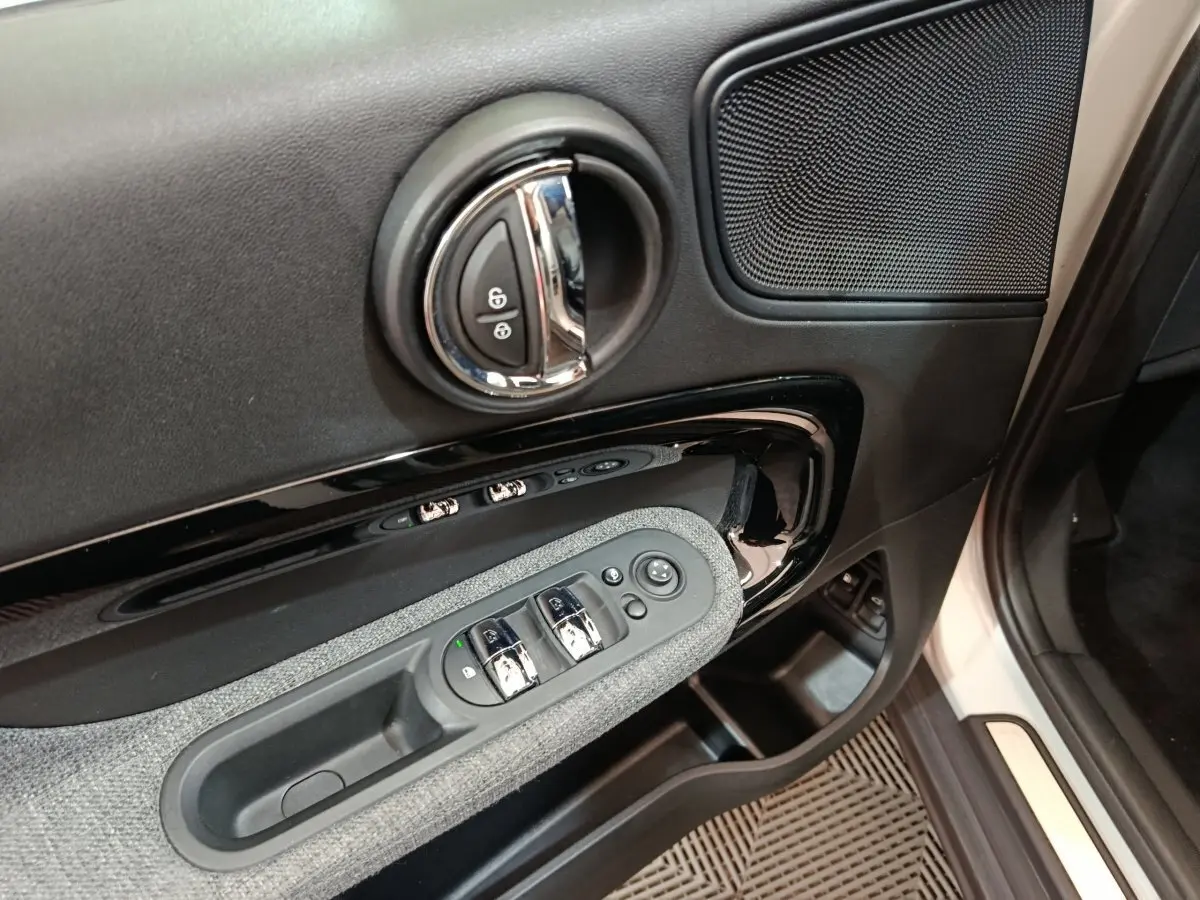 Gros plan sur la porte côté conducteur du MINI Countryman blanc, montrant les commandes de vitres et la poignée chromée.