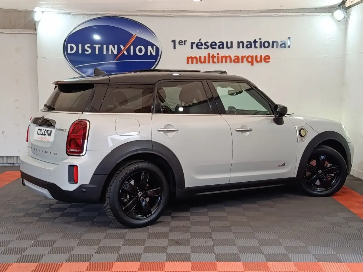 Vue latérale droite d'un MINI Countryman Cooper SE blanc avec toit noir et jantes noires en intérieur showroom.
