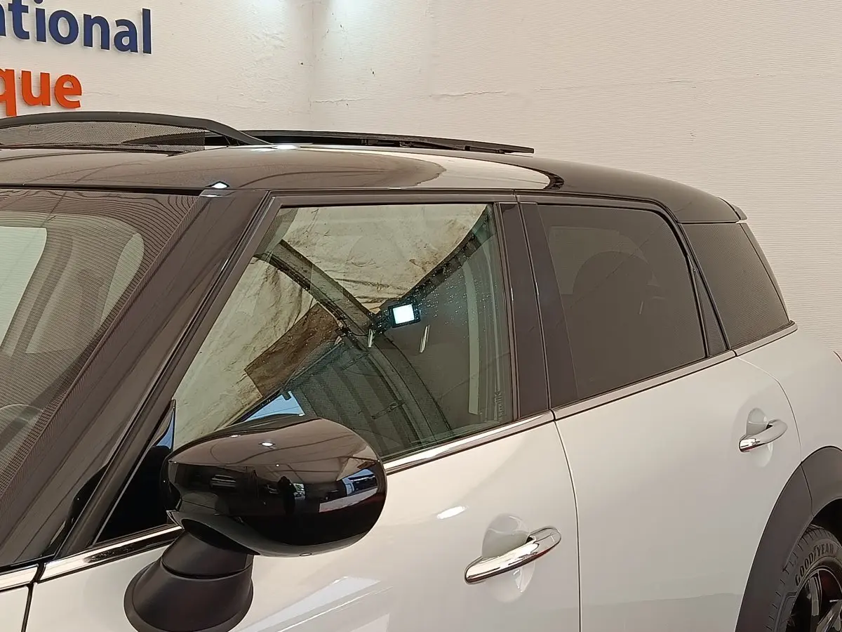 Vue latérale gauche d'une MINI Countryman hybride rechargeable blanche avec toit noir et rétroviseur noir brillant.