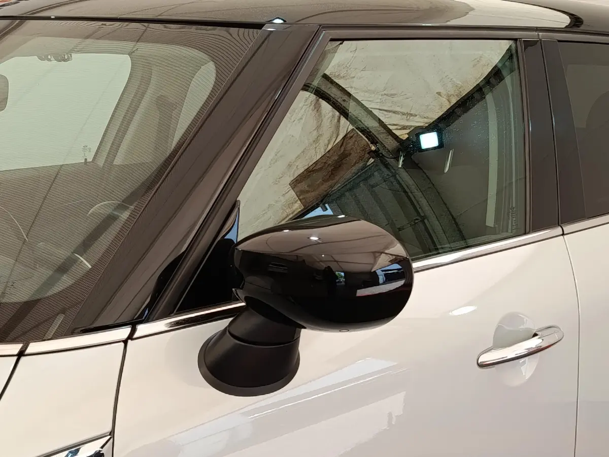 Gros plan sur le rétroviseur noir côté gauche d'une MINI Countryman blanche avec porte et vitre teintée.