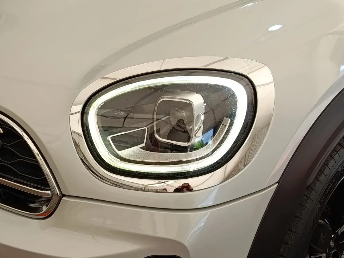 Gros plan sur le phare avant droit LED du MINI Countryman Cooper SE blanc, soulignant son design moderne et lumineux.