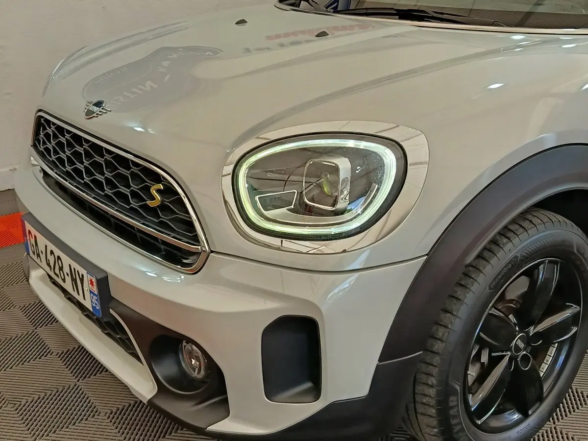 Vue 3/4 avant droit d'un MINI Countryman Cooper SE blanc avec phares LED et jantes noires brillantes.