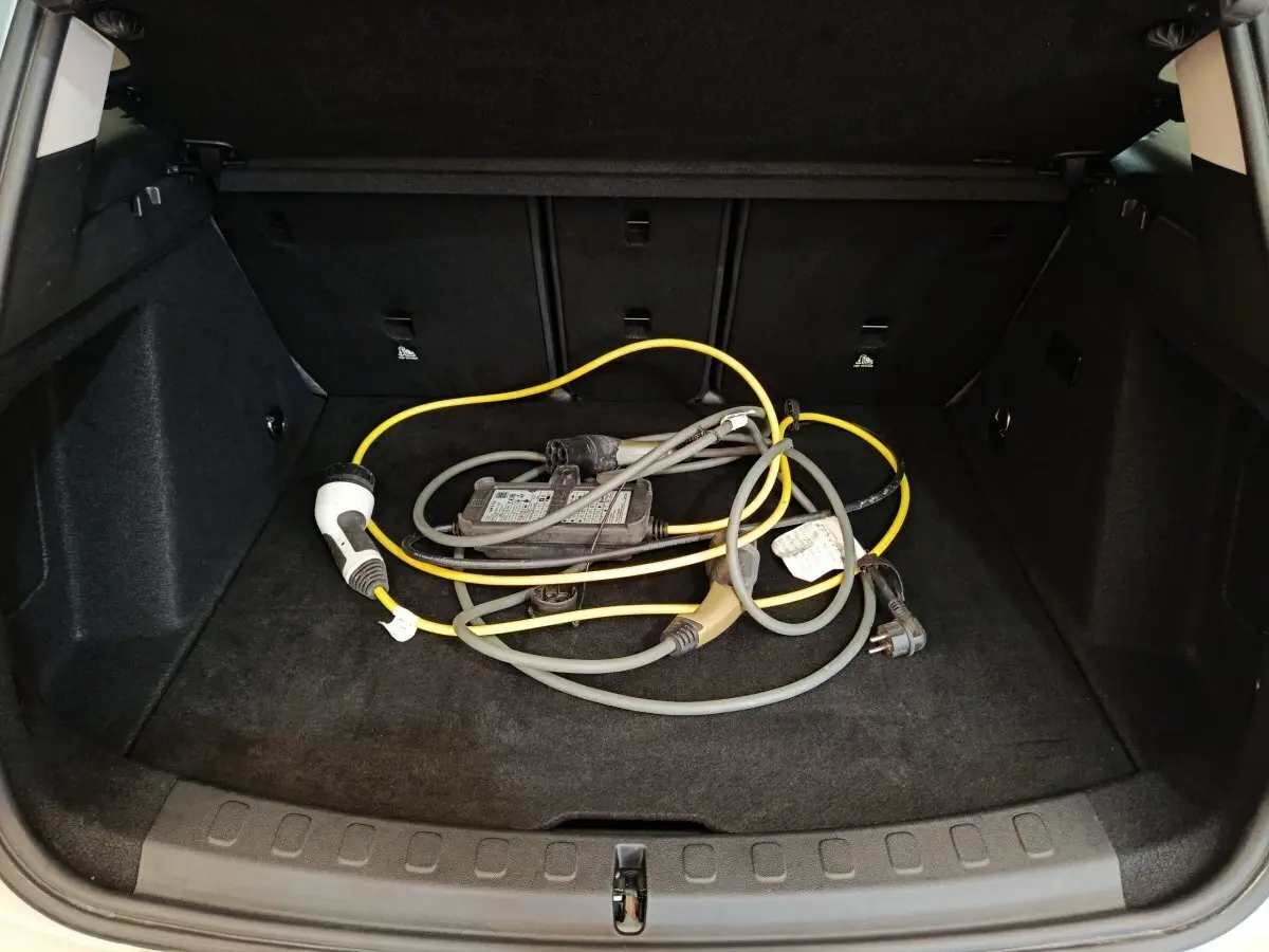 Coffre ouvert d'une MINI Countryman blanche 2021 montrant un câble de recharge hybride posé sur la moquette noire.