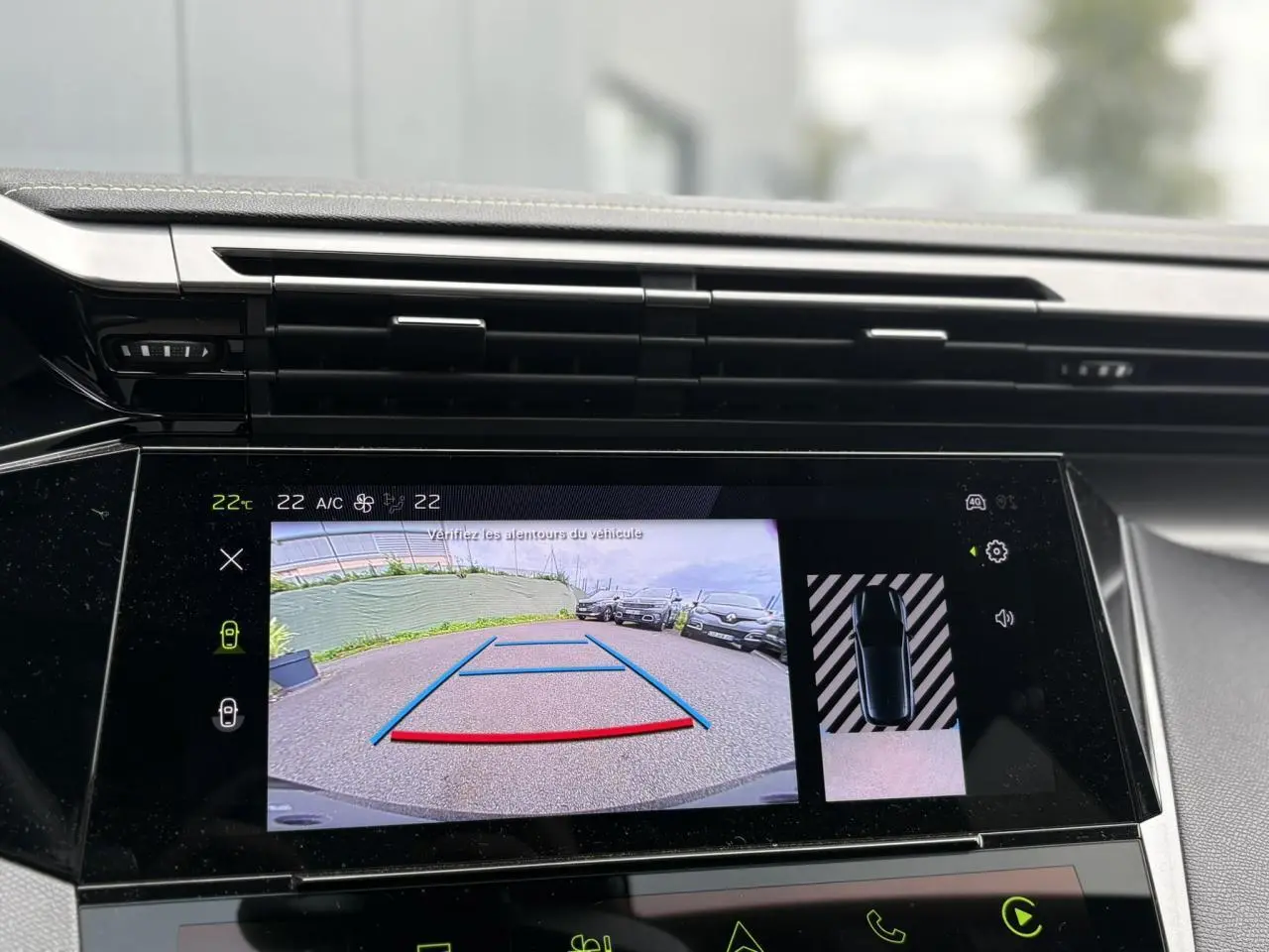 Écran central tactile montrant la caméra de recul et l'aide au stationnement d'une Peugeot 308 blanche Okenite.