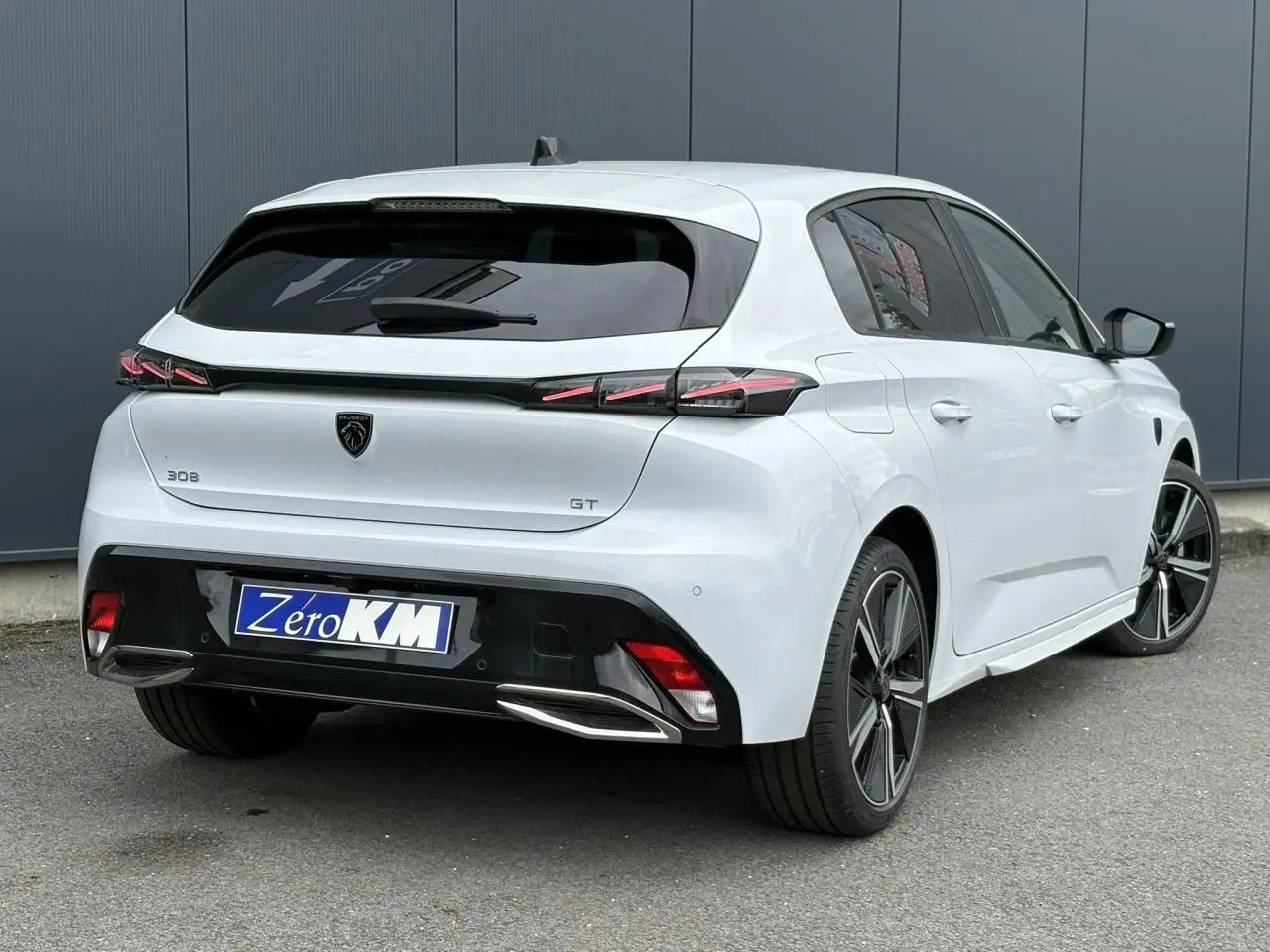 Vue 3/4 arrière droite d'une Peugeot 308 GT blanche Okenite avec feux LED et jantes alliage 18 pouces.