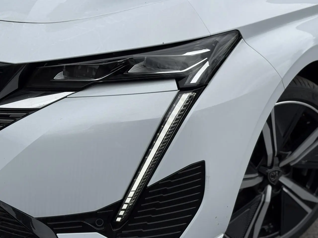 Gros plan sur le phare avant gauche blanc Okenite du Peugeot 308 2024 avec jante alliage 18 pouces diamantée.