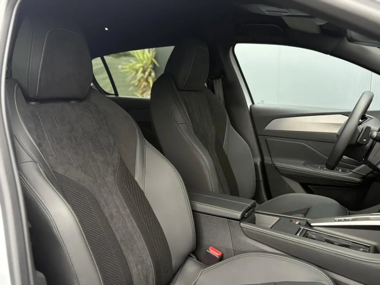 Intérieur de la Peugeot 308 2024, vue côté gauche, sièges avant en sellerie tri matières noire avec surpiqûres blanches.