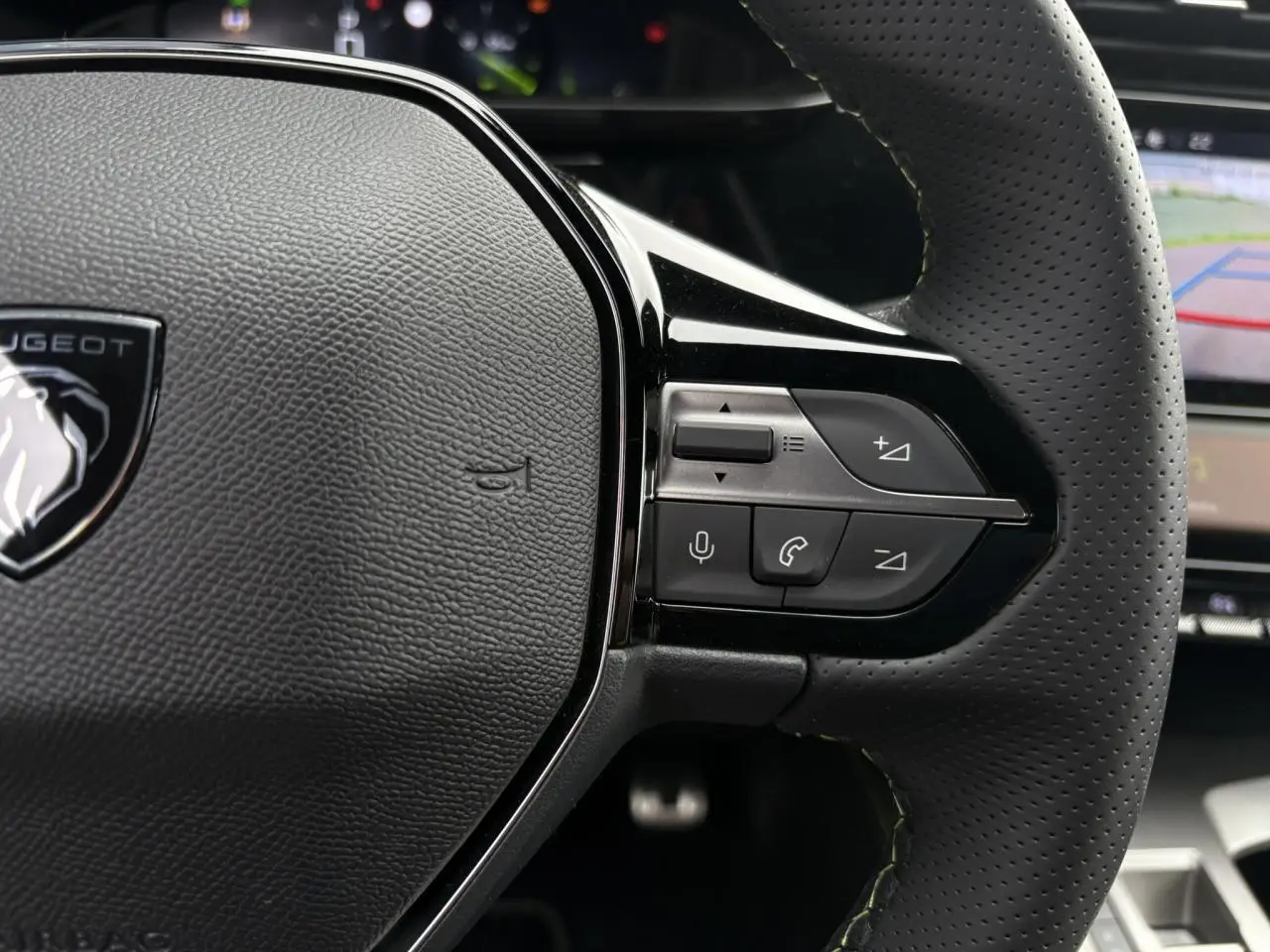 Gros plan sur le volant cuir perforé de la Peugeot 308 2024, avec commandes vocales et téléphone intégrées.