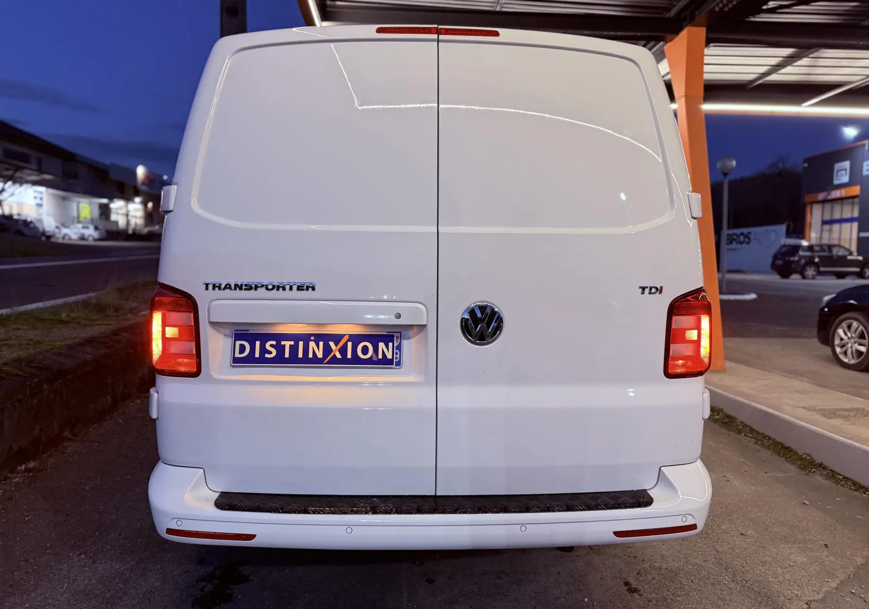 Vue arrière d’un Volkswagen Transporter blanc L1H1 2.0 TDI 150 avec feux allumés et plaque Distinxion.