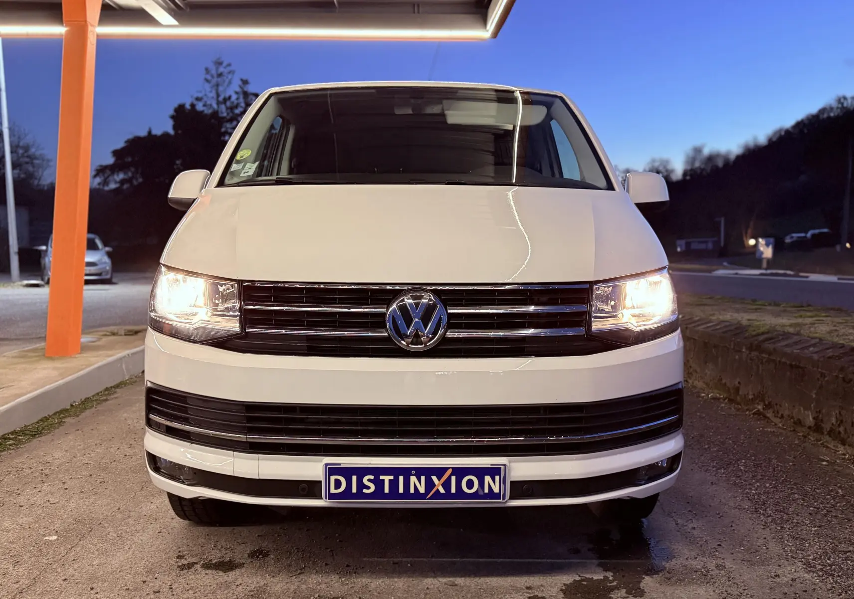 Vue avant d’un Volkswagen Transporter L1H1 blanc de 2018 avec phares allumés et plaque Distinxion visible.