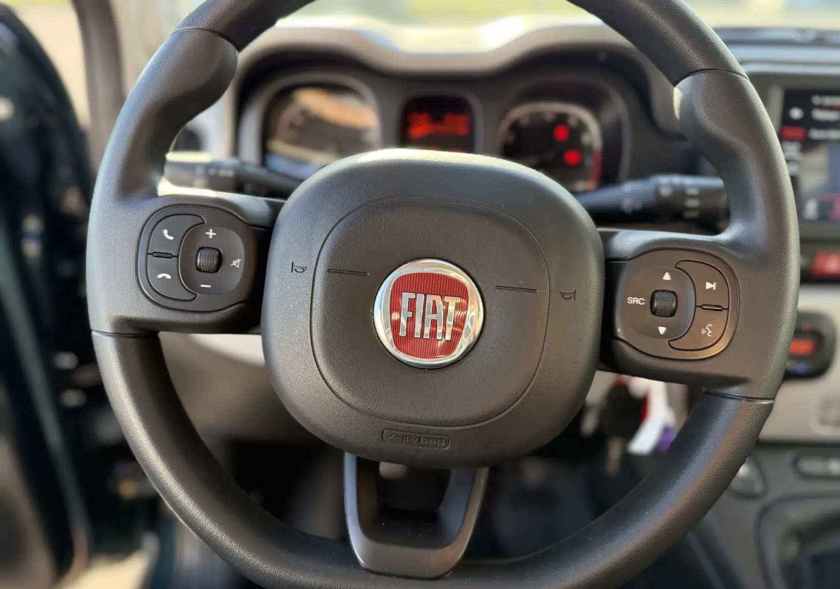 Gros plan sur le volant noir de la Fiat Panda City Cross 2023 avec commandes intégrées et logo rouge central.