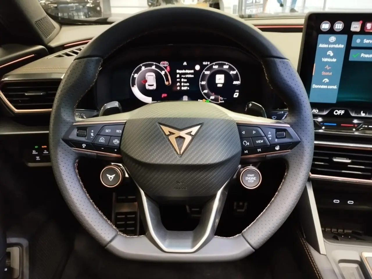 Vue intérieure centrée sur le volant perforé noir avec logo CUPRA cuivré et tableau de bord digital lumineux.
