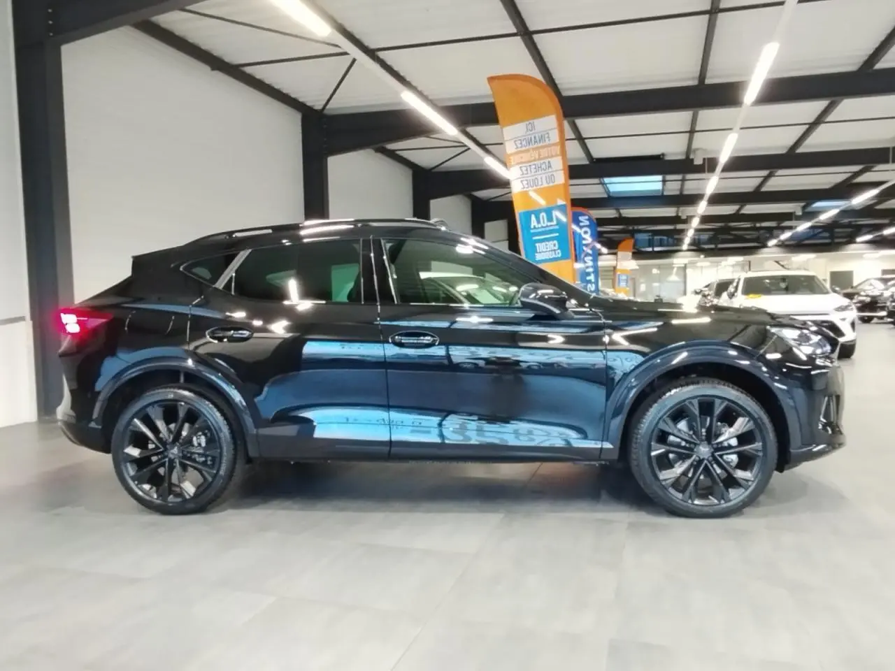 Vue de profil côté gauche d'une CUPRA Formentor noire métal avec jantes alliage noires dans un showroom.