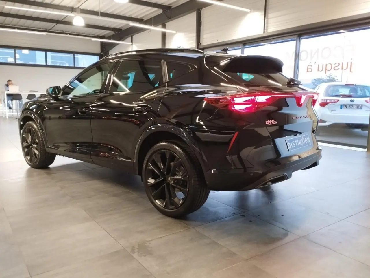 Vue 3/4 arrière droite du CUPRA Formentor noir métal avec jantes noires et feux arrière allumés en intérieur showroom.