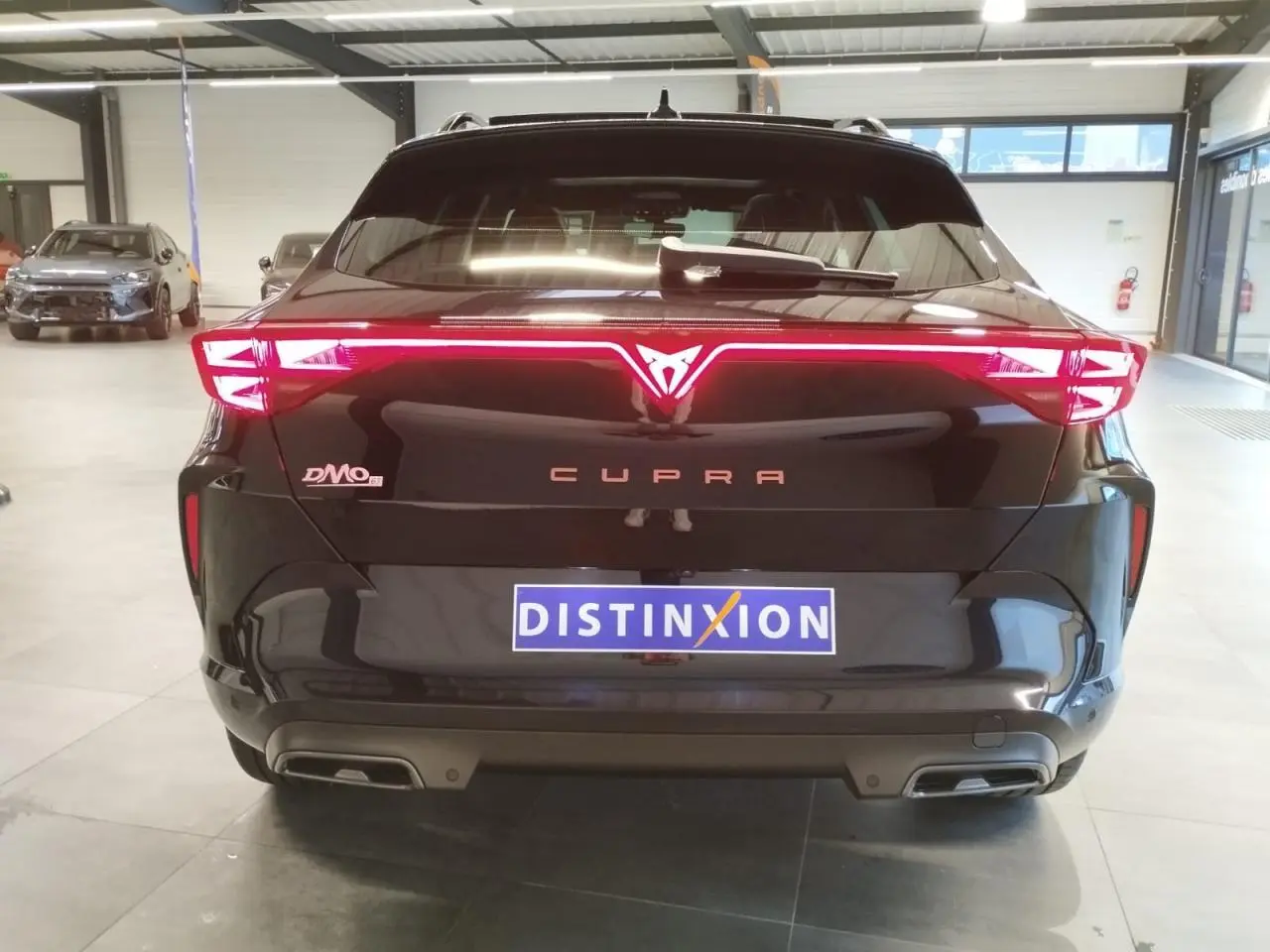 Vue arrière d'une CUPRA Formentor noire métallisée avec feux arrière Tri-LED allumés en intérieur showroom.