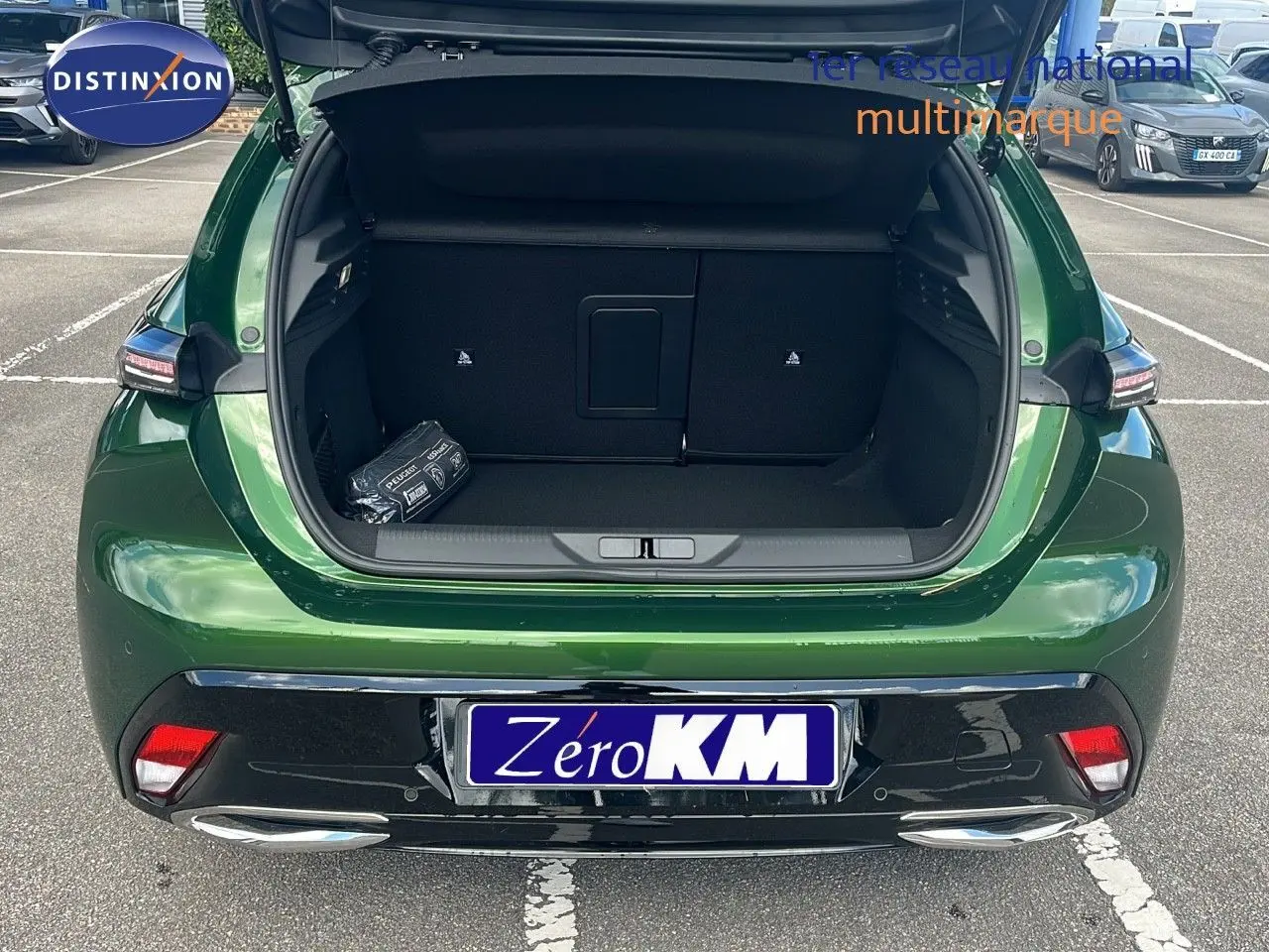 Vue arrière d'une Peugeot 308 1.2 Hybrid 136ch Allure en vert olivine métal avec coffre ouvert sur parking.
