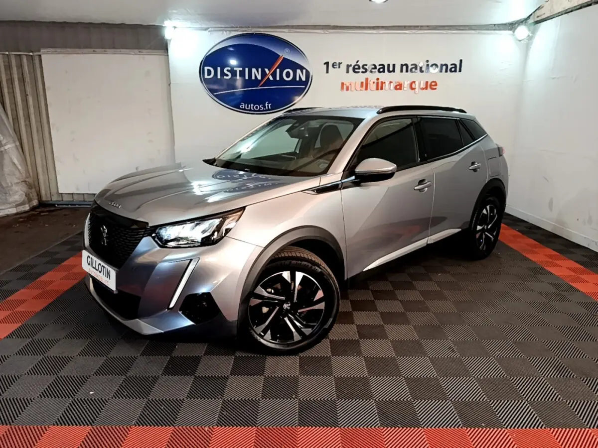 Peugeot 2008 gris clair en 3/4 avant droit, avec jantes noires et toit noir dans un showroom.