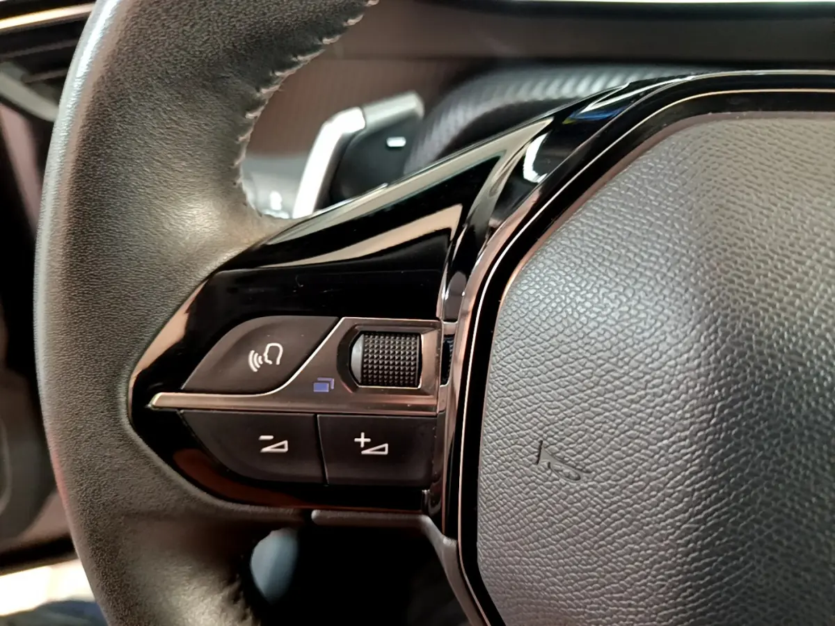 Gros plan sur les commandes vocales et volume du volant cuir noir du Peugeot 2008 gris clair, version 2021.