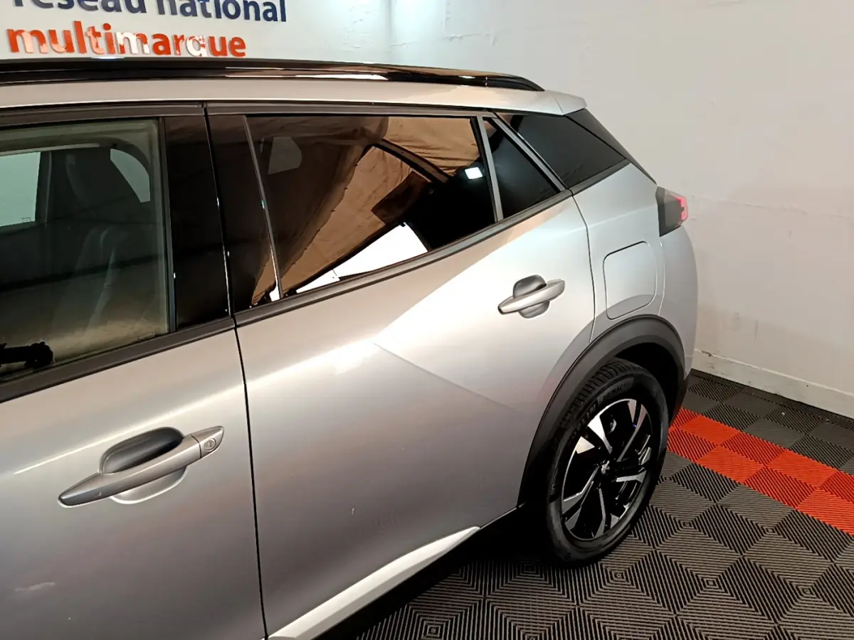 Vue côté droit arrière d'un Peugeot 2008 gris clair avec jante noire et toit noir contrasté dans un intérieur showroom.