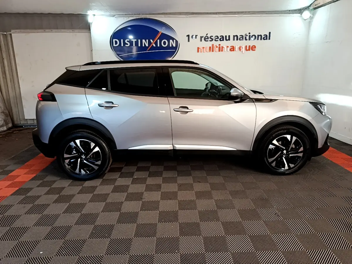 Profil côté gauche d'un Peugeot 2008 gris clair stationné en intérieur avec jantes noires et toit panoramique.