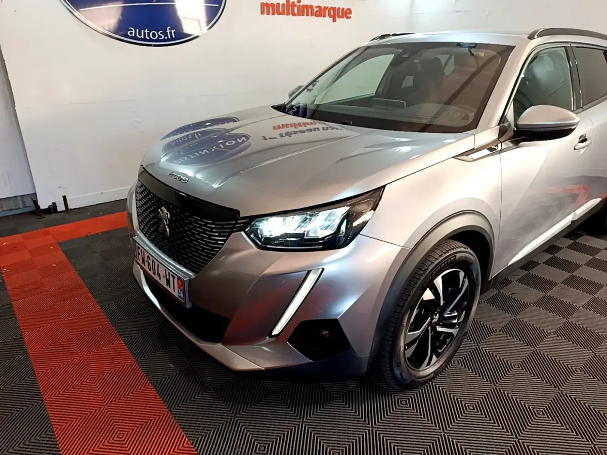Peugeot 2008 gris clair vue 3/4 avant droit avec phares LED allumés et jantes noires brillantes.