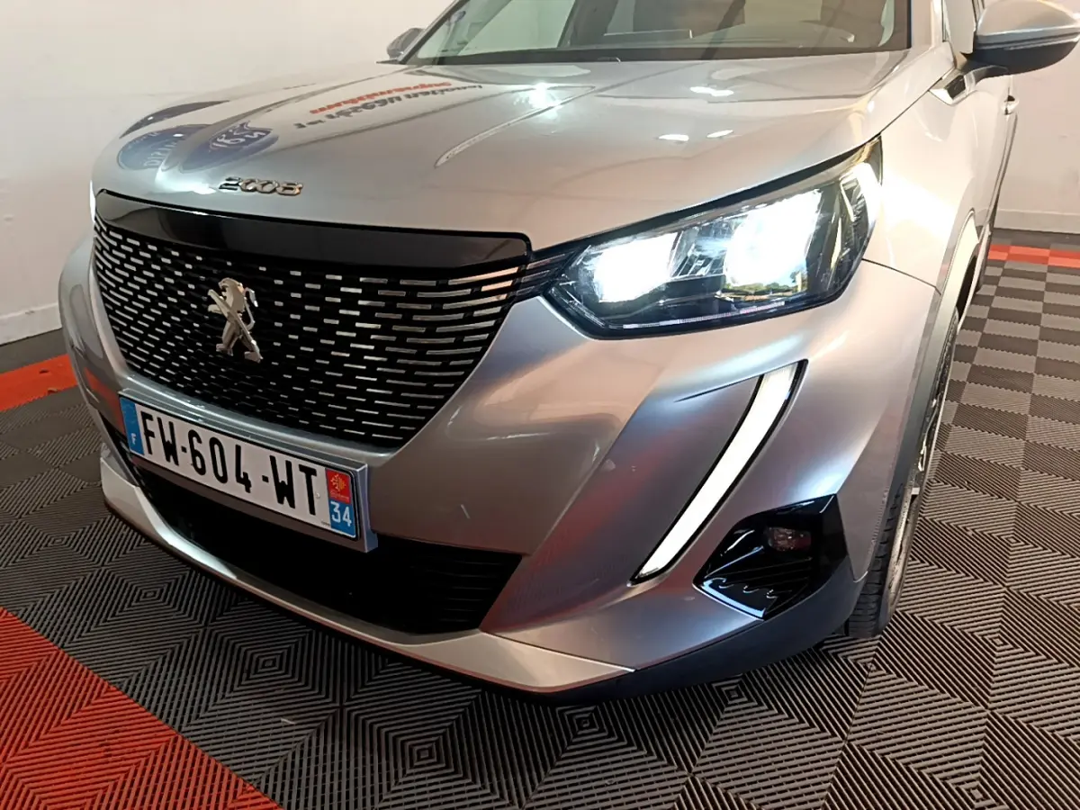 Vue 3/4 avant droit d'un Peugeot 2008 gris clair avec phares LED allumés et calandre noire distinctive.