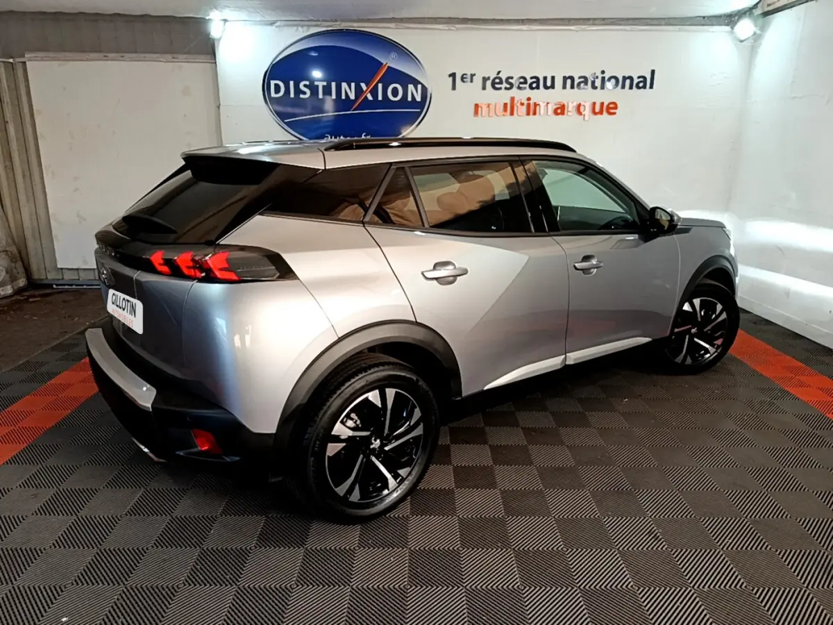 Peugeot 2008 gris clair vue 3/4 arrière droit, avec feux arrière LED et jantes noires distinctives.