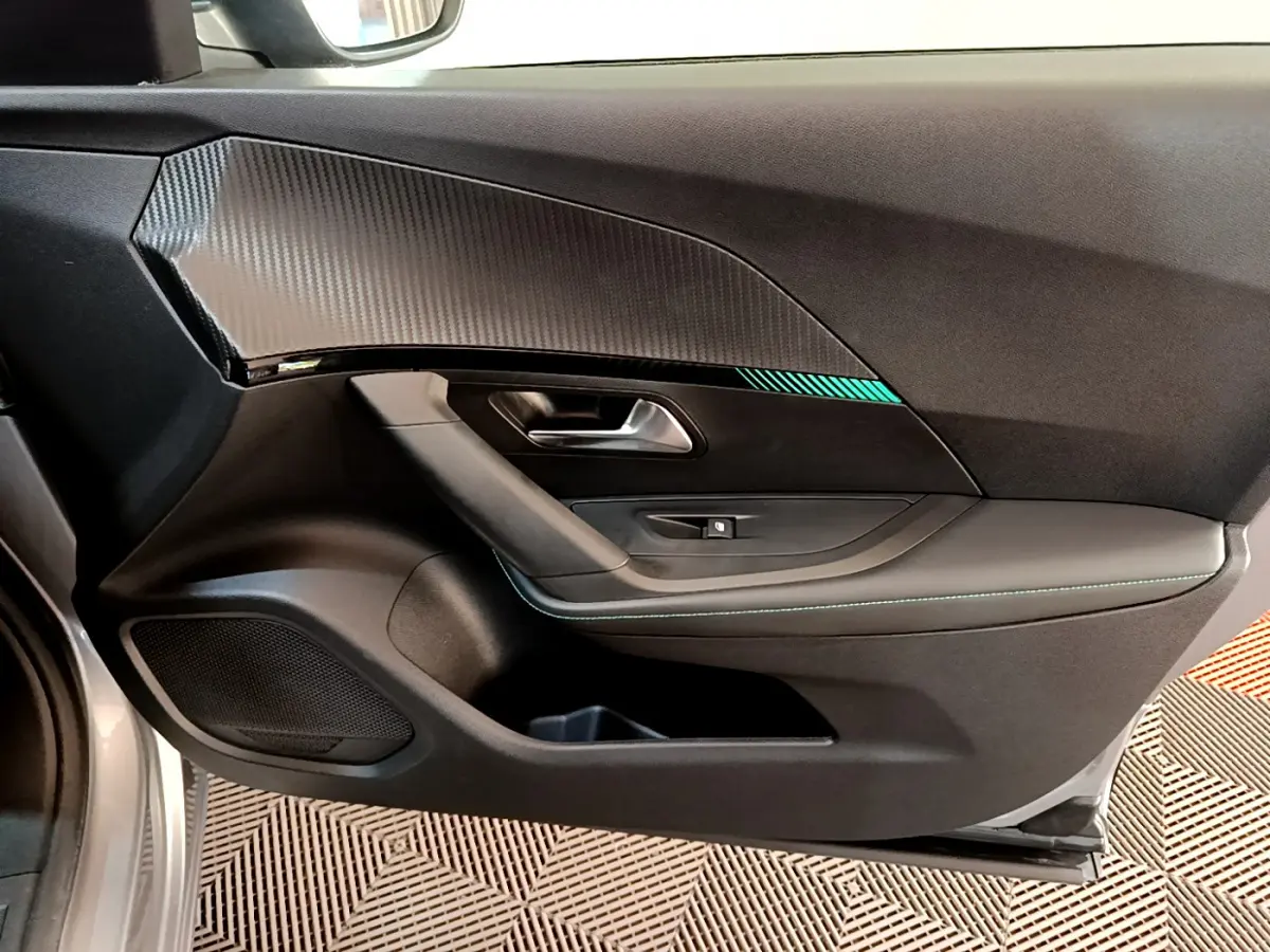Vue intérieure côté gauche de la porte avant d'une Peugeot 2008 gris clair avec insert décoratif noir et surpiqûres vertes.