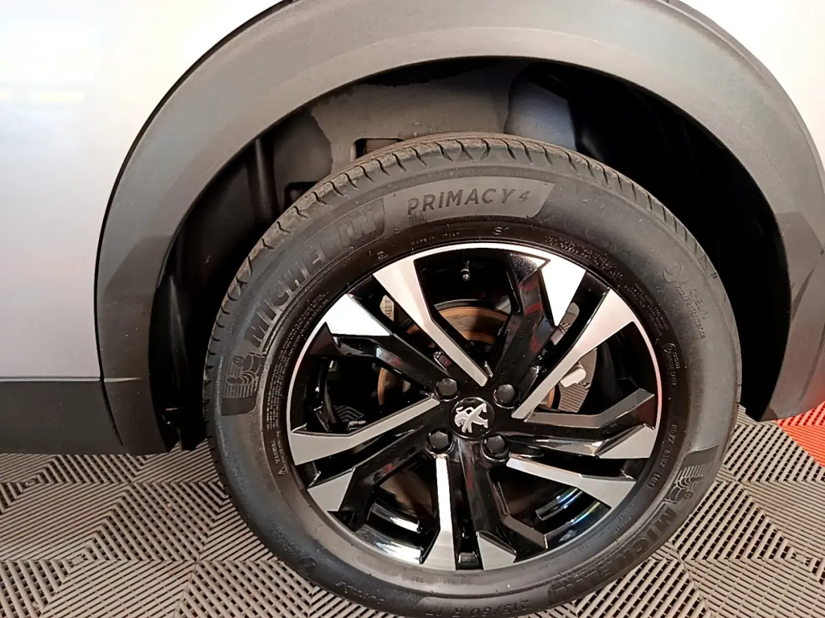 Gros plan sur la roue avant gauche du Peugeot 2008 gris clair, avec jante alliage noire et argentée au design moderne.