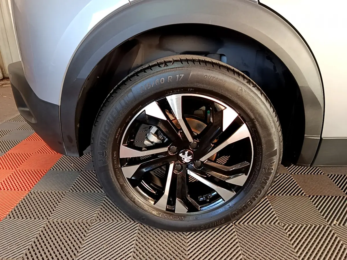 Gros plan sur la roue avant gauche du Peugeot 2008 gris clair, mettant en valeur la jante alliage noire et argentée.