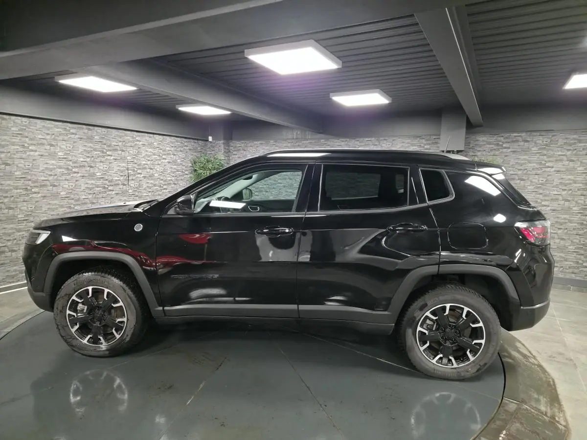 Jeep Compass Trailhawk noir en profil côté gauche, avec jantes alliage 17'' et vitres surteintées dans un garage.