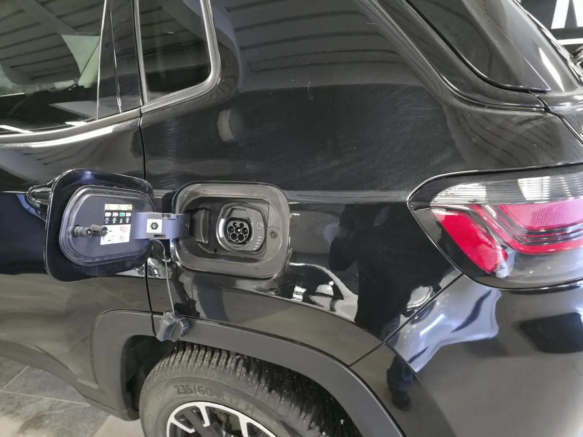 Prise de recharge ouverte côté gauche sur Jeep Compass Trailhawk noir 2024, avec feu arrière et jante visible.