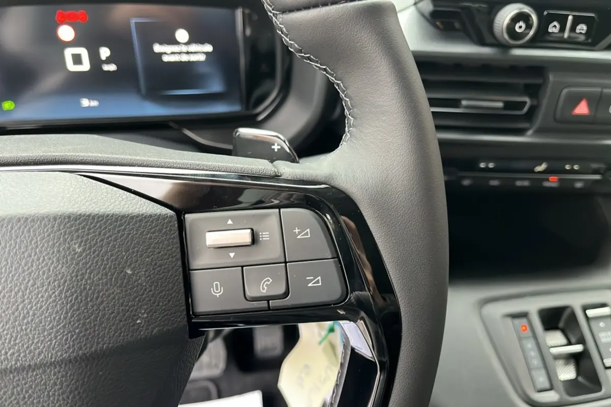 Gros plan sur le volant cuir noir multifonctions du Citroën Berlingo 2026 avec commandes audio et écran digital en arrière-plan.