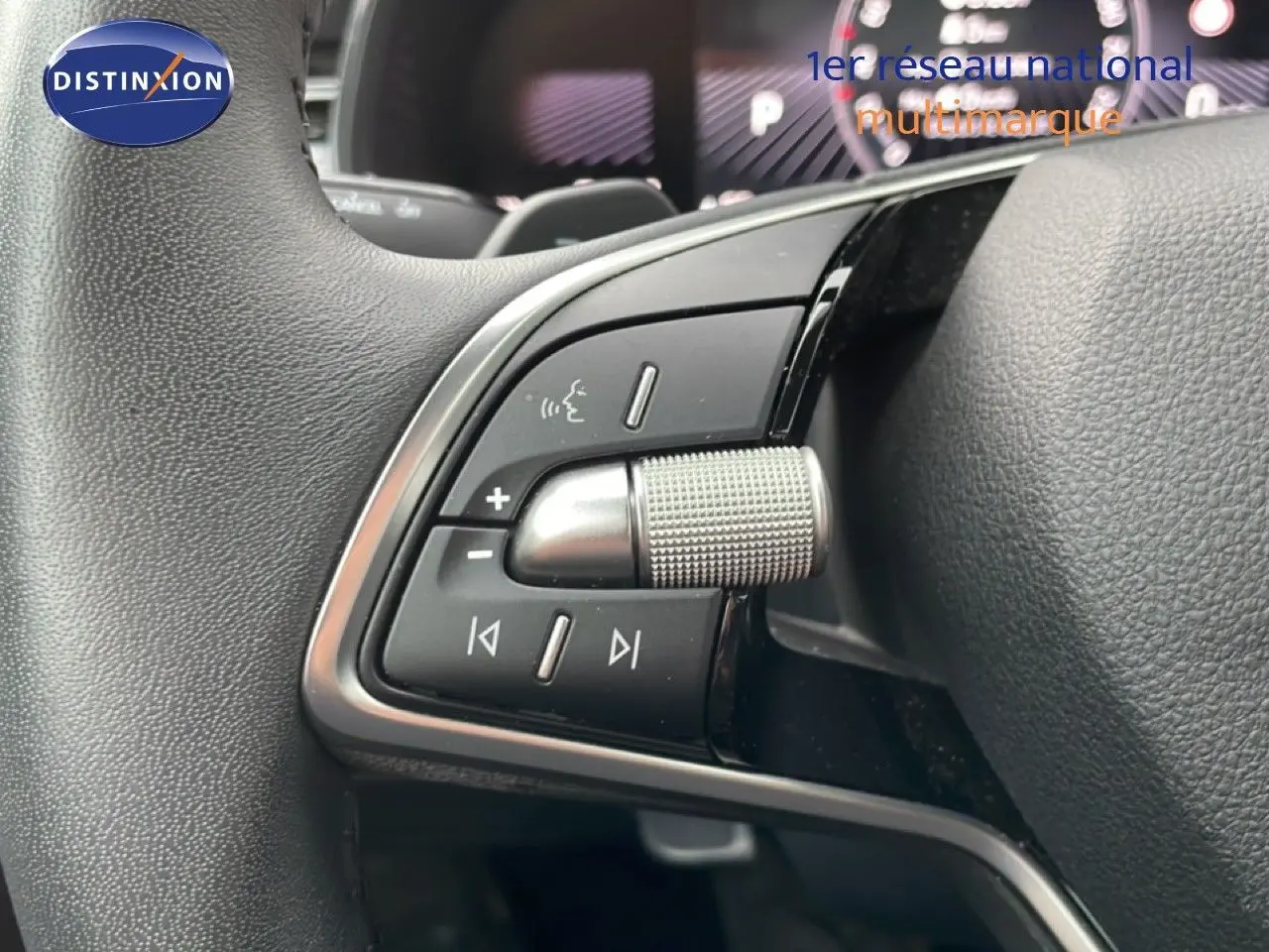 Gros plan sur les commandes multimédia au volant d’un Skoda Kamiq blanc glacier, avec molette texturée et boutons noirs.