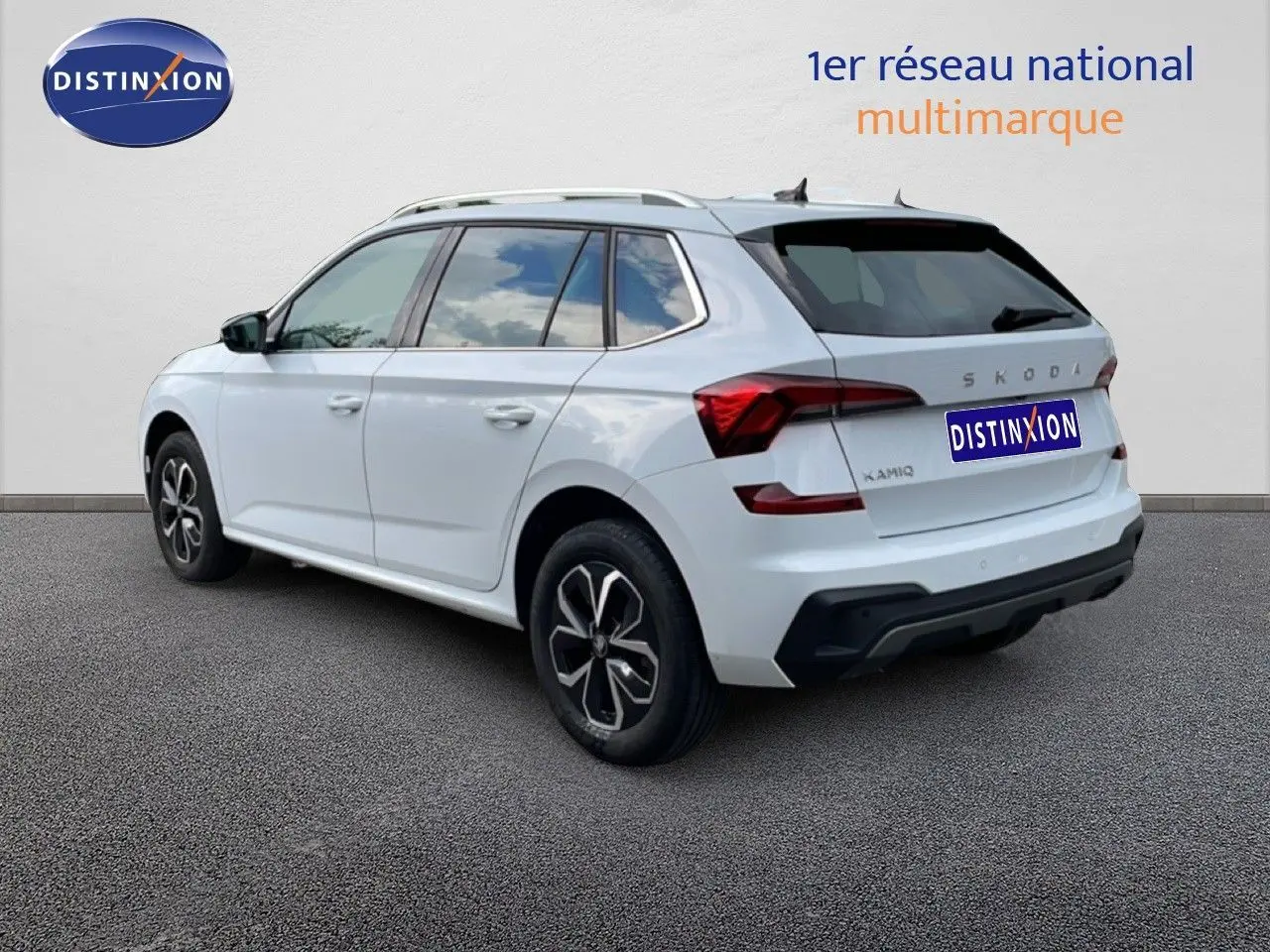 Vue 3/4 arrière droite d'un Skoda Kamiq blanc glacier avec jantes noires et toit ouvrant, sur fond neutre.