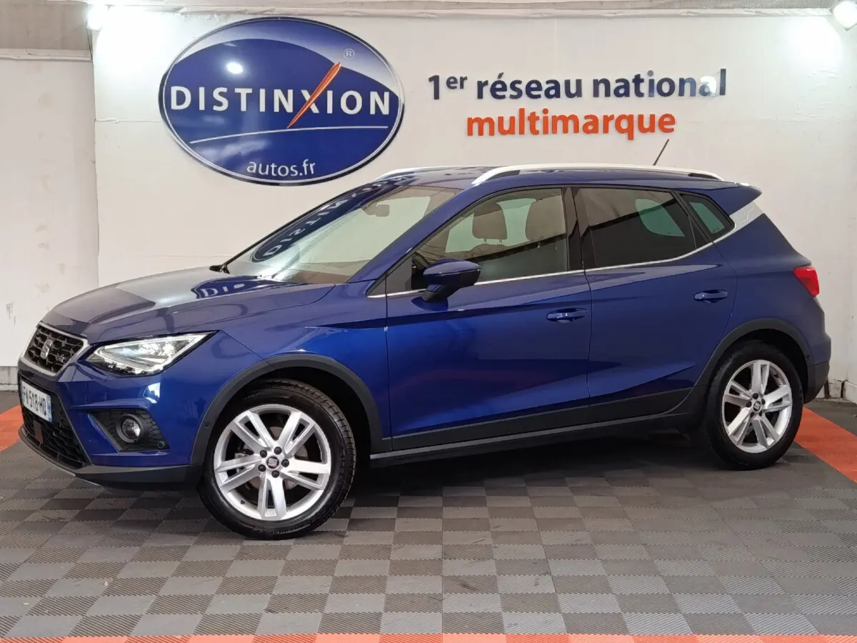 SEAT Arona bleu en vue profil côté gauche, SUV compact avec jantes alliage et barres de toit chromées.