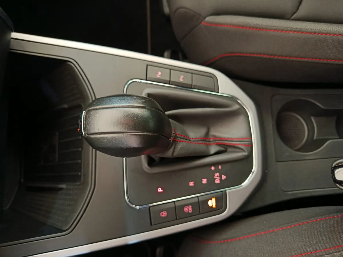 Gros plan sur la console centrale de la SEAT Arona 2021, levier de vitesses automatique avec coutures rouges et sièges tissu noirs.