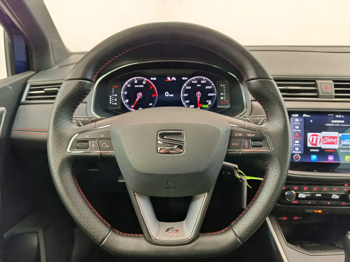 Vue intérieure centrée sur le volant cuir noir avec surpiqûres rouges du SEAT Arona FR 2021 et tableau de bord digital.