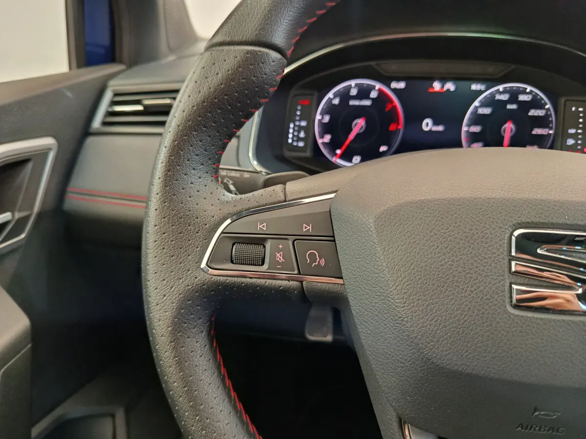 Gros plan sur le volant cuir noir avec surpiqûres rouges et tableau de bord numérique de la SEAT Arona 2021.