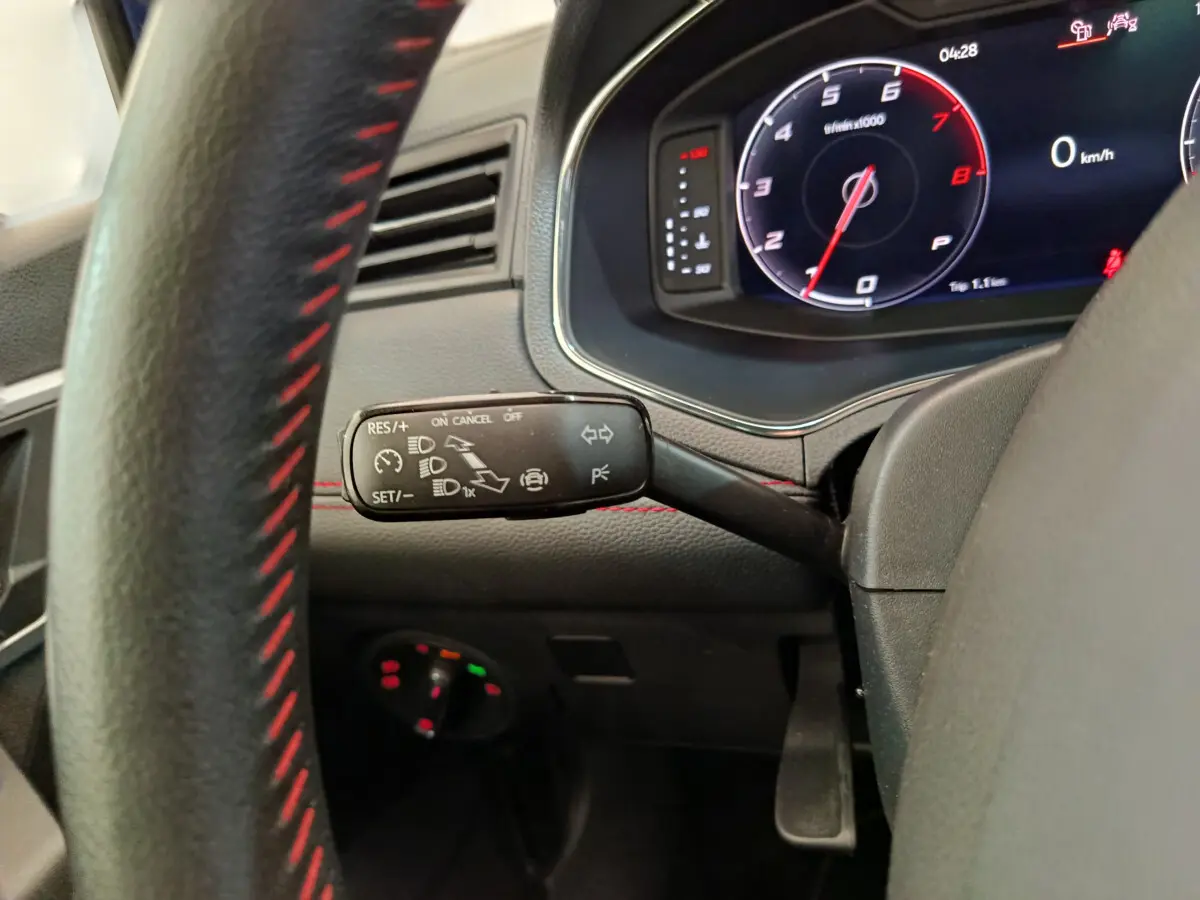 Gros plan sur la manette de régulateur de vitesse et le tableau de bord numérique du SEAT Arona 2021, intérieur noir avec surpiqûres rouges.