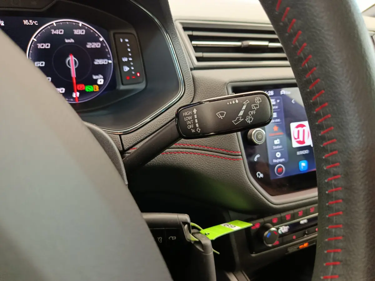 Vue rapprochée du commodo d’essuie-glace à gauche sur le tableau de bord noir avec surpiqûres rouges d’un SEAT Arona bleu 2021.