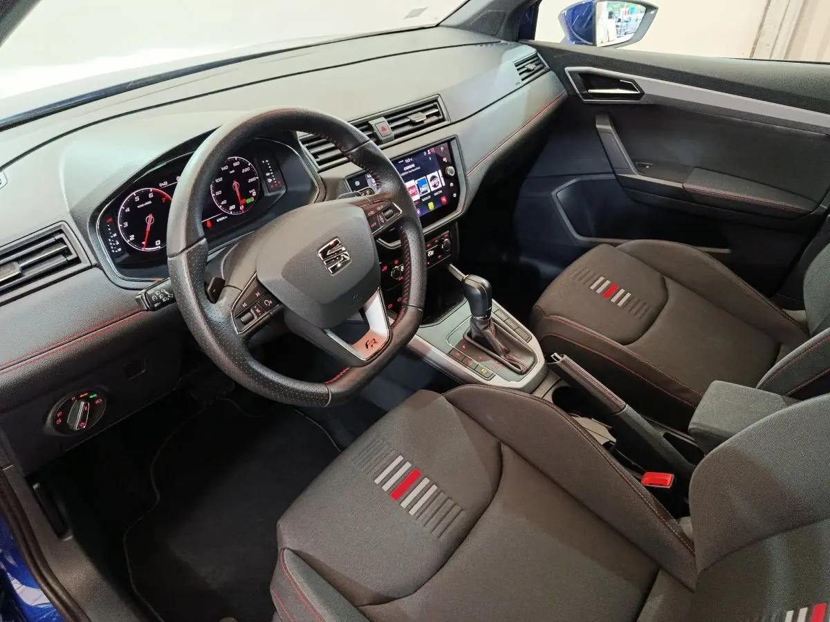 Intérieur du SEAT Arona 2021 vu côté conducteur, volant cuir, sièges noirs avec surpiqûres rouges et console centrale avec boîte auto.