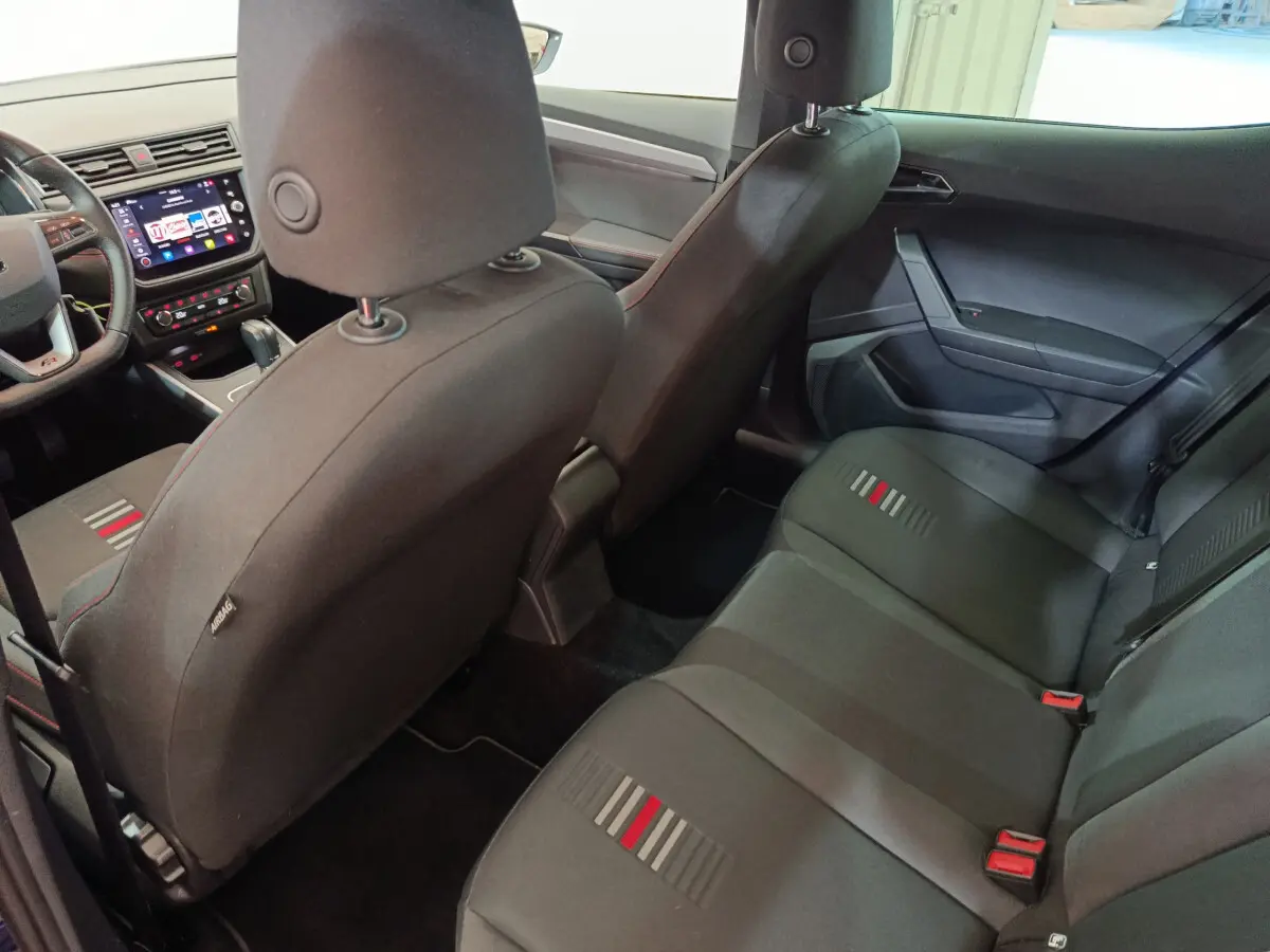 Vue intérieure arrière de la SEAT Arona 2021, sièges tissu noirs avec motifs rouges et gris, tableau de bord visible côté conducteur.