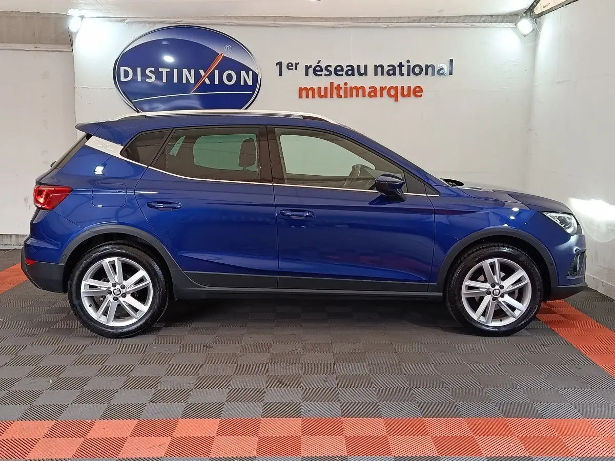 Profil côté gauche d'un SUV SEAT Arona bleu 2021 avec jantes alliage et toit noir en intérieur showroom.