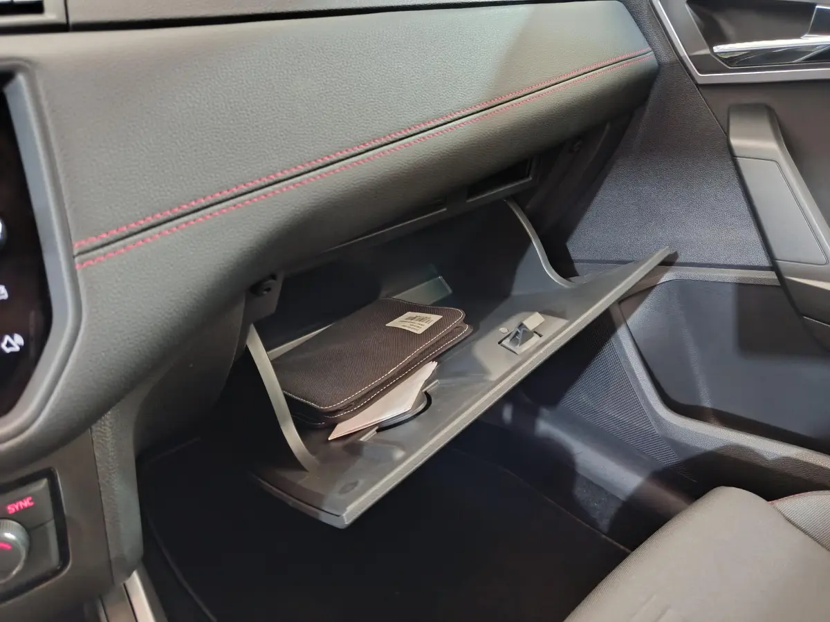 Vue intérieure côté passager du coffre à gants ouvert d'une SEAT Arona bleu 2021, avec surpiqûres rouges et pochette noire visible.