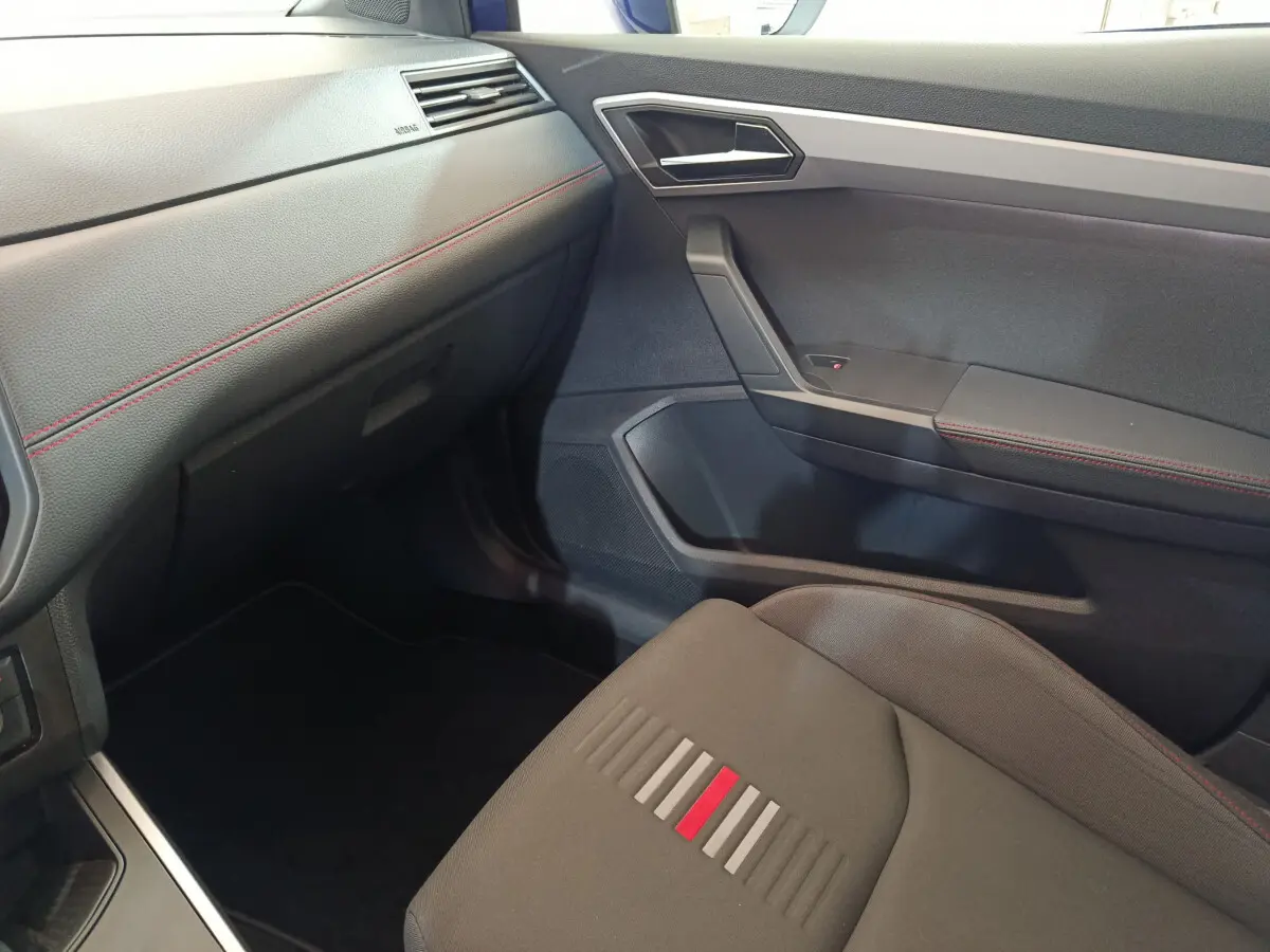 Intérieur côté passager de la SEAT Arona 2021, avec sièges gris et surpiqûres rouges, tableau de bord noir texturé.