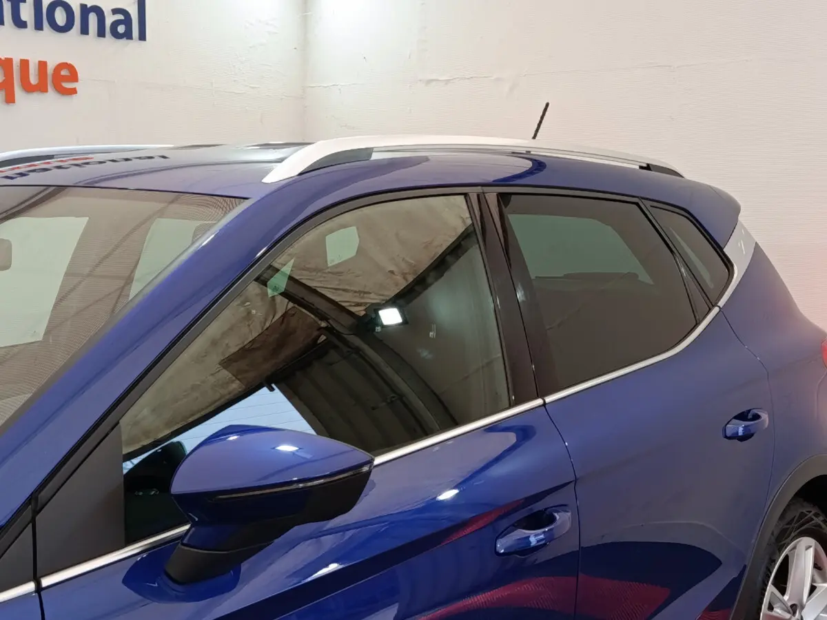 Vue de profil côté gauche du SEAT Arona bleu 2021, soulignant les rétroviseurs et barres de toit chromées.
