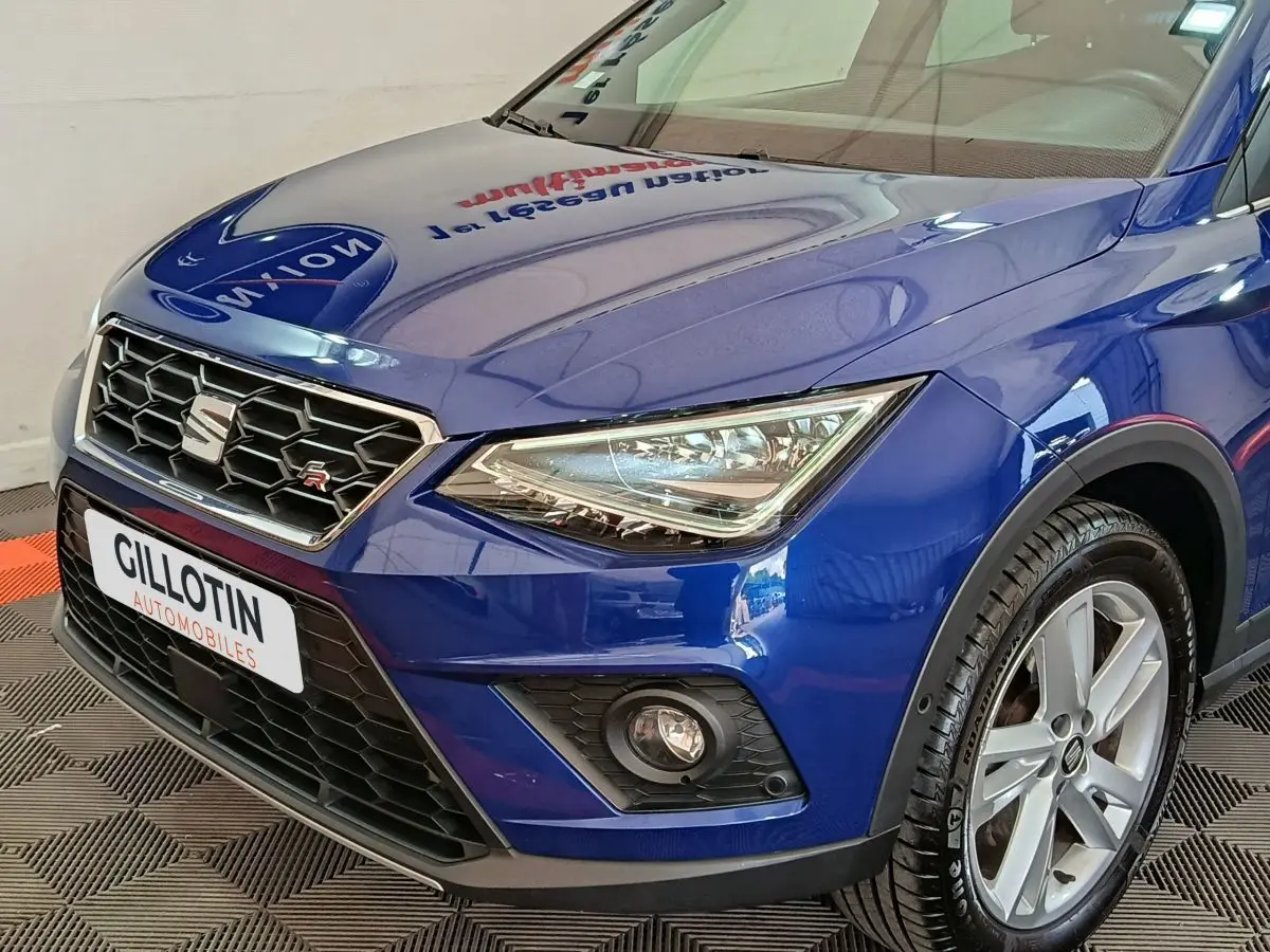 Vue 3/4 avant droite d'une SEAT Arona bleu profond avec calandre hexagonale et phares LED anguleux.