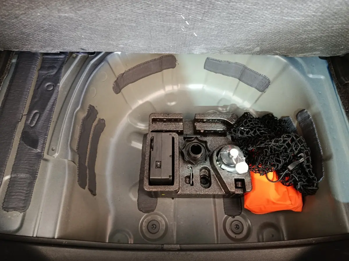 Vue plongeante sur le coffre vide d'une SEAT Arona bleu 2021, montrant le rangement sous tablette avec kit de bord.