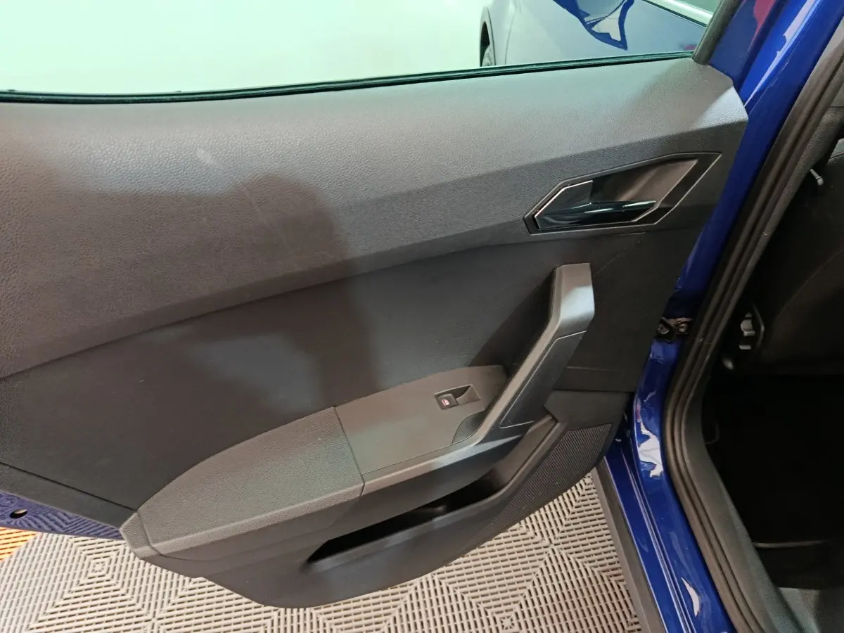 Vue rapprochée de la porte arrière gauche bleu vif d'une SEAT Arona 2021, avec poignée et commande de vitre noire.